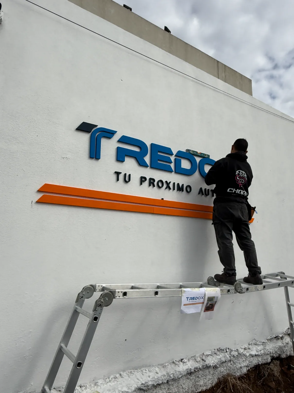 Hombre colocando el logo corpóreo de Tredo en pared exterior